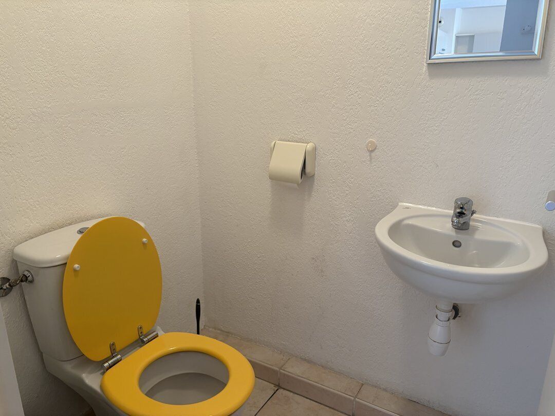 A bathroom with a yellow toilet, a white sink, and a roll of toilet paper on the wall.