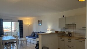 Ein kompakter Wohnraum mit Essbereich, einer Couch, einer Küche mit Schränken und einem Mülleimer.