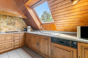 A kitchen with wooden cabinets, a granite countertop, a built-in dishwasher, and a window with a view of trees. - Homerez - Apartment in Epfig (Epfig)