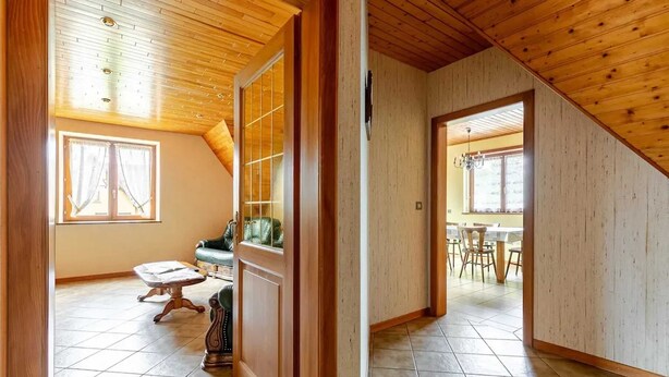 A spacious room with a wooden ceiling, a dining area with a table and chairs, and a large window with curtains.