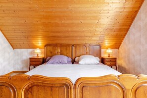 A bedroom with a wooden ceiling, a four-poster bed, two bedside tables with lamps, and floral wallpaper. - Homerez - Apartment in Epfig (Epfig)