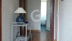 Um corredor com parede branca, luminária azul sobre prateleira branca e porta no final.