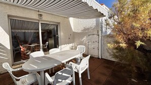 Un patio al aire libre con una mesa y sillas, un área cubierta y un ventanal corredizo que da a un espacio interior.