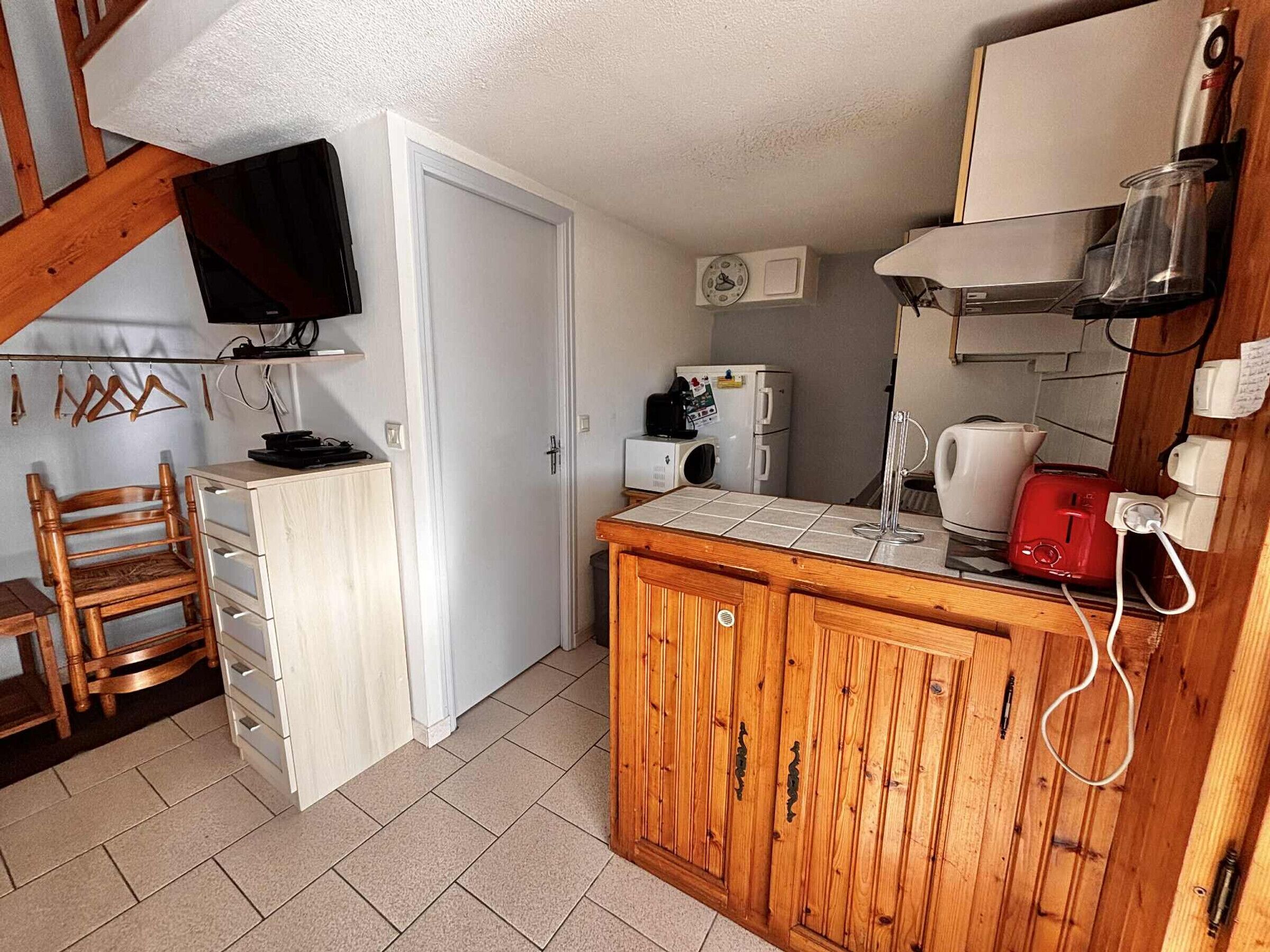 Eine kompakte Küche mit Holzausstattung, einem integrierten Fernseher, einer Kaffeemaschine und einem Toaster.