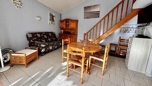 Una sala de estar con una mesa de comedor de madera, sillas, un sofá, una escalera y una zona de cocina.