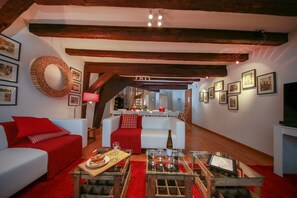 Un salon chaleureux avec une cheminée, des meubles rouges et blancs, et un coin repas à l’arrière-plan.
