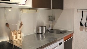 Et lille tekøkken med en stålgrå bordplade, indbygget opvaskemaskine og vask.