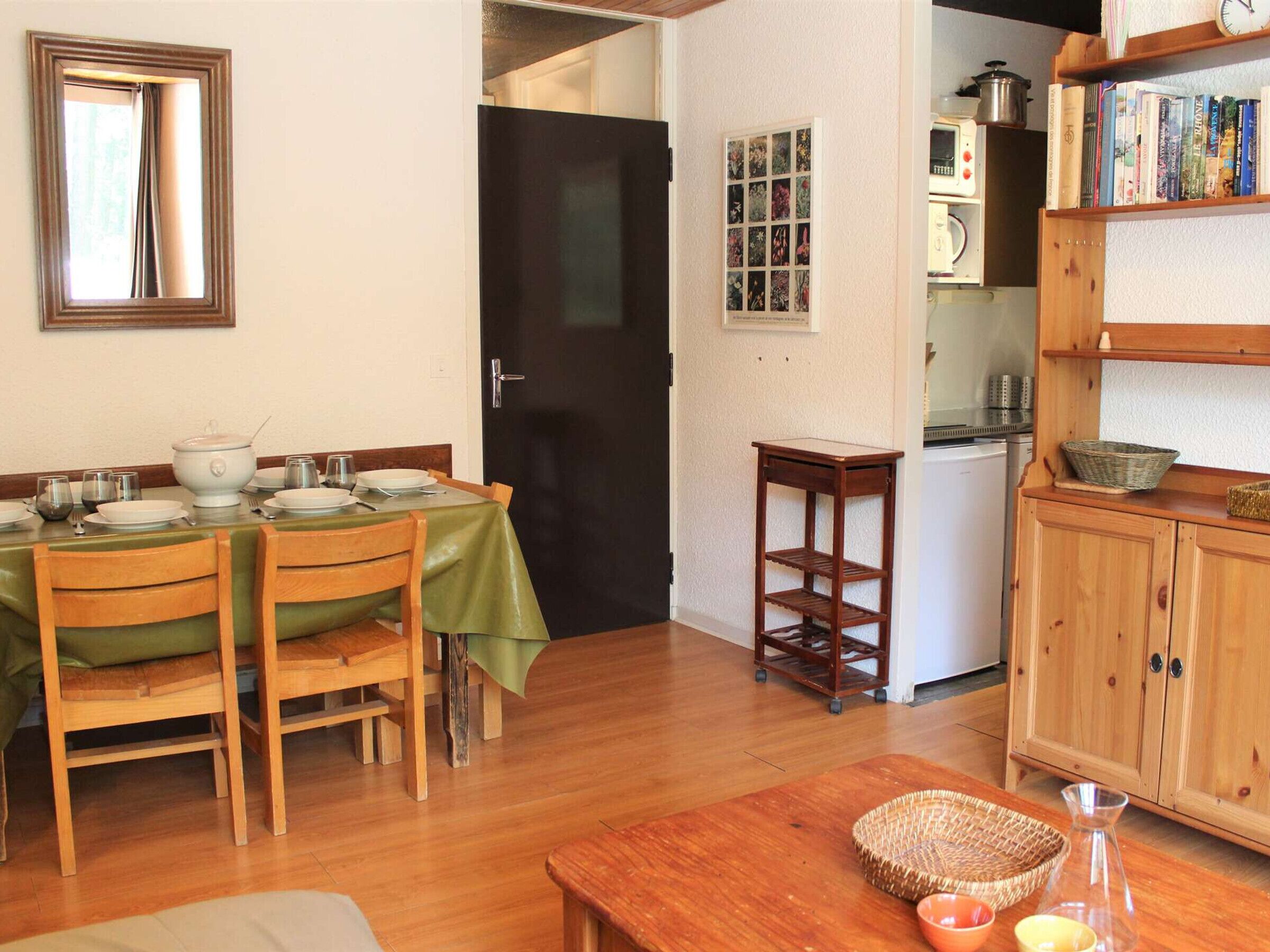 A dining area with a table set for four, wooden chairs, a small side table, and a cabinet with shelves.