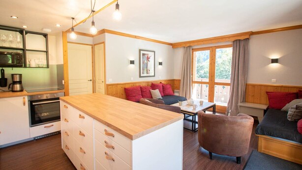 A cozy, well-lit room with a wooden dining table, a sofa, and a bed. There is a kitchen area with a microwave and a coffee maker. - Large 5-bedroom apartment Valmorel, pets allowed, parking (Valmorel)