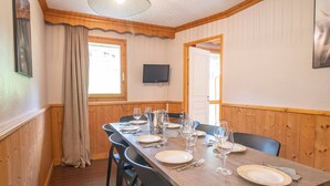 A dining room with a wooden table set for six, chairs, a television on the wall, and a window with curtains. - Large 5-bedroom apartment Valmorel, pets allowed, parking (Valmorel)