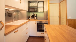 A compact kitchen with white cabinets, wooden countertops, a built-in microwave, and a stove. - Large 5-bedroom apartment Valmorel, pets allowed, parking (Valmorel)