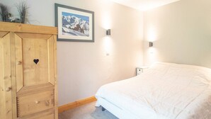 A bedroom with a bed, a wooden wardrobe, a framed picture on the wall, and two wall-mounted lights. - Large 5-bedroom apartment Valmorel, pets allowed, parking (Valmorel)