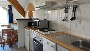 A compact kitchen with a stove, microwave, and sink. There is a wooden table and chairs in the adjacent dining area. - Cozy apartment with balcony, slope access, 6 people, Peyresourde (Peyragudes)