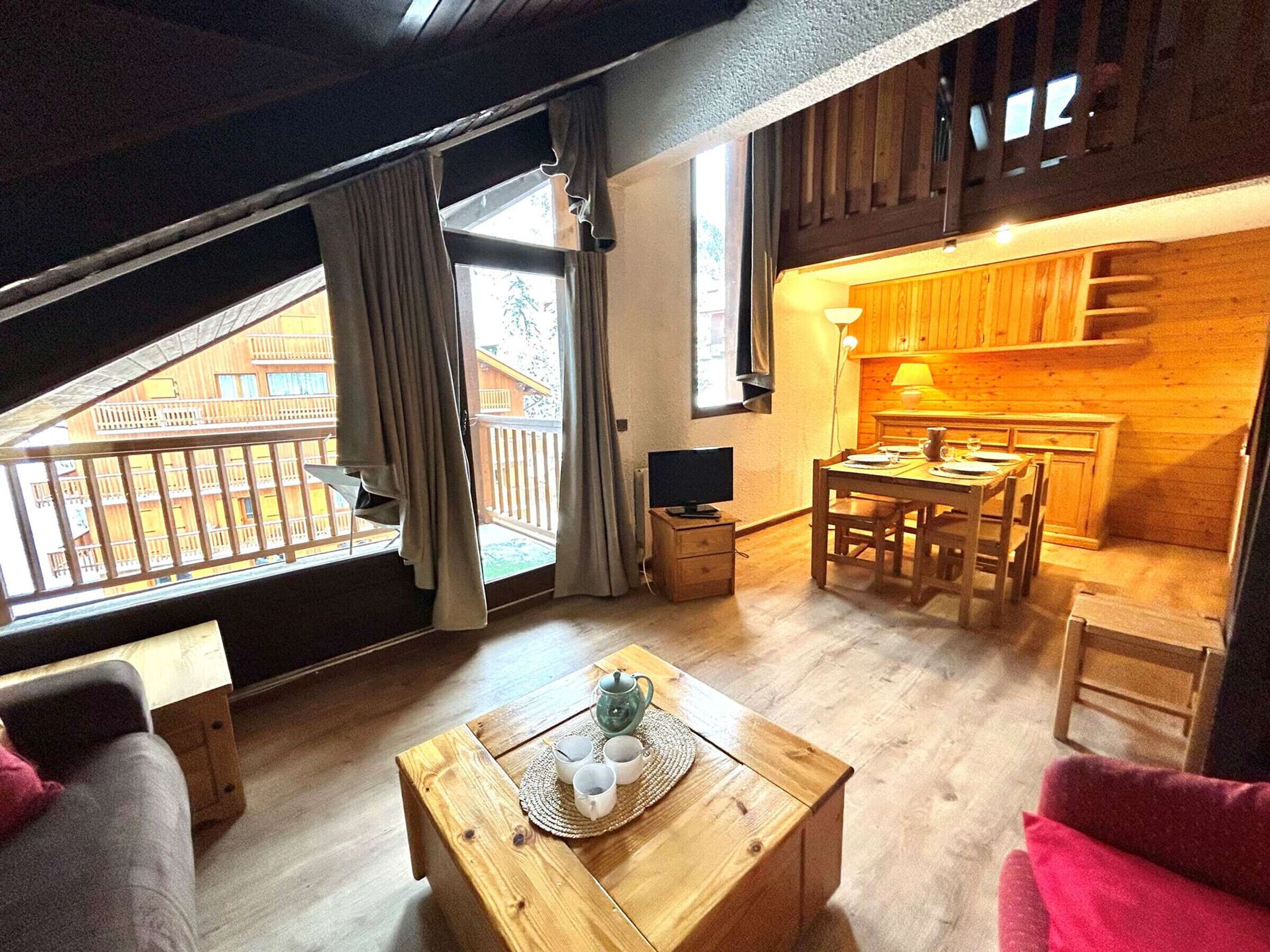 A cozy loft-style room with a dining area, wooden floors, and a view of a balcony.