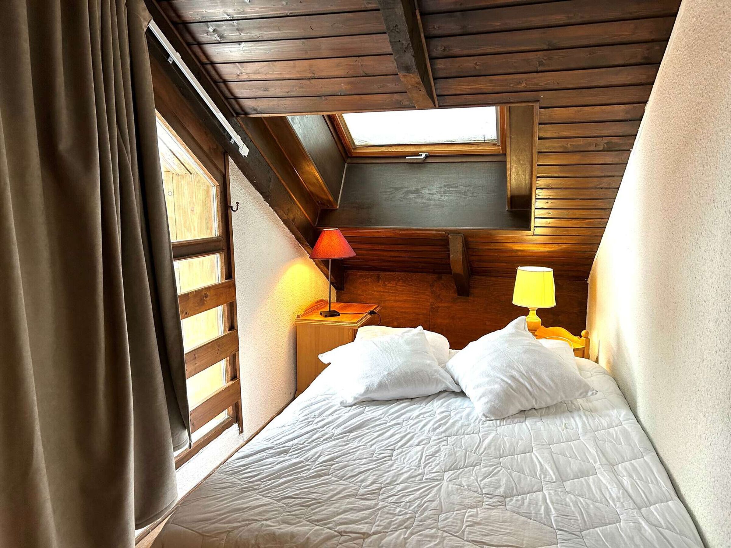 A bedroom with a bed, a nightstand, a lamp, and a window.
