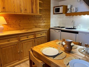 A wooden kitchen with a dining table set for two, a microwave, and a coffee maker on the wall.