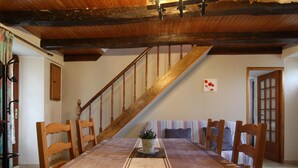Un espace repas comprenant une longue table, des chaises en bois, un escalier et une porte dotée de panneaux en verre dépoli.