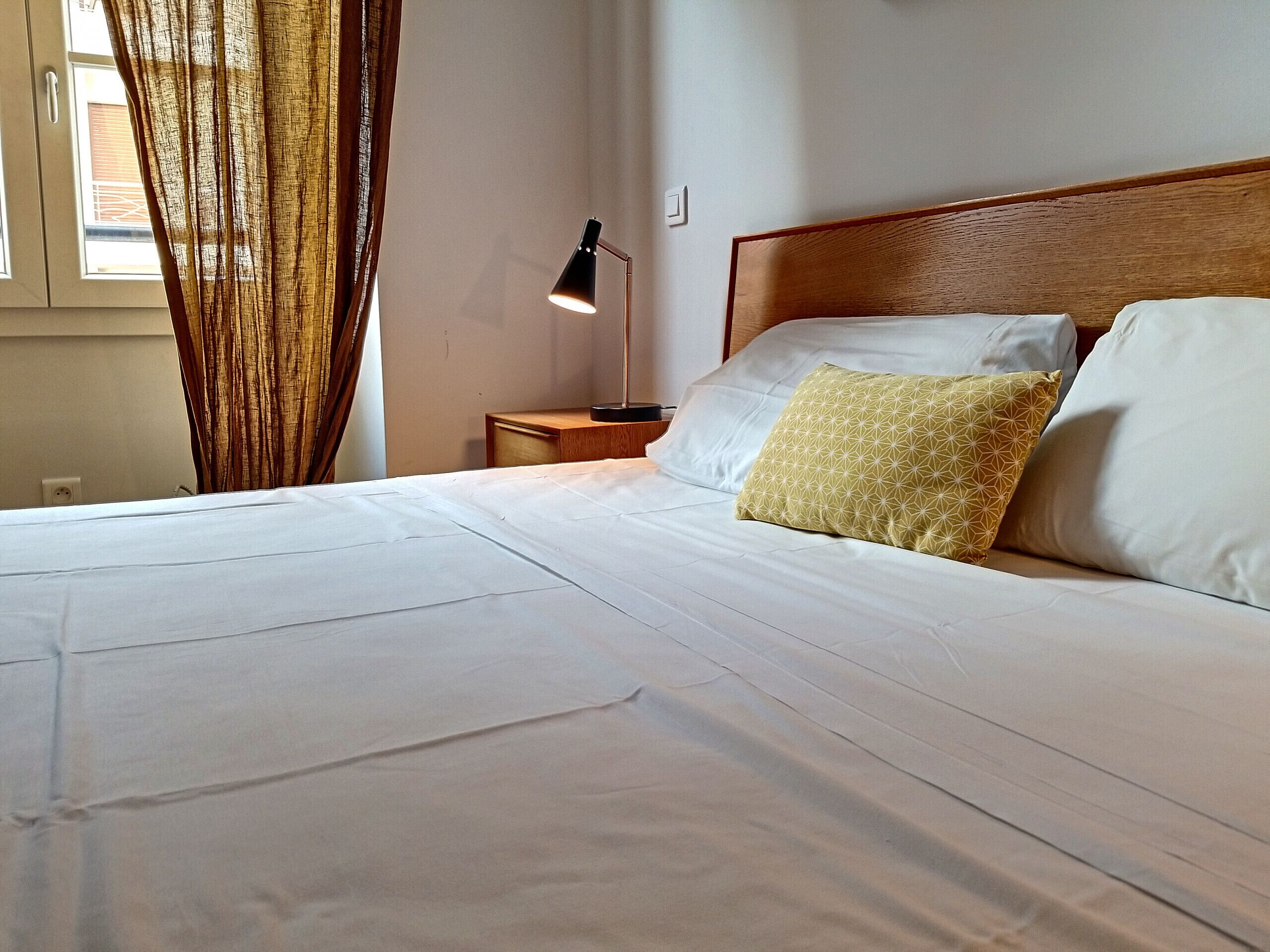 A neatly made bed with white linens, a wooden headboard, and a bedside table with a lamp.