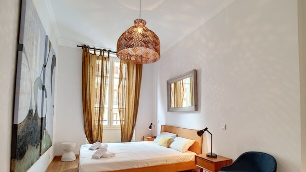A bedroom with a wooden bed, a hanging light fixture, a chair, and a window with curtains. - N&J - COLIBRI PRESTIGE - Central - By sea (Niza)