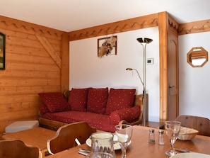 Une pièce chaleureuse avec un mur en bois, un canapé rouge agrémenté de coussins à motifs, une table avec des chaises et un lampadaire.