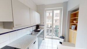 A modern kitchen with white cabinets, a granite countertop, and a view of a balcony with buildings.