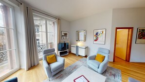 A modern living room with two grey armchairs, a coffee table, a TV, and a small side table.
