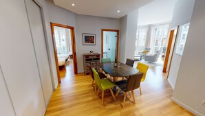 A dining area with a wooden table and chairs, a small cabinet, and a painting on the wall.