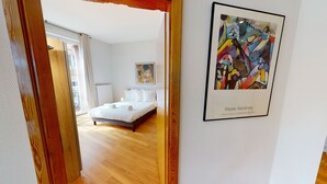A hotel room with a bed, a painting, and a view of the outside.