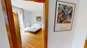 A hotel room with a bed, a painting, and a view of the outside.