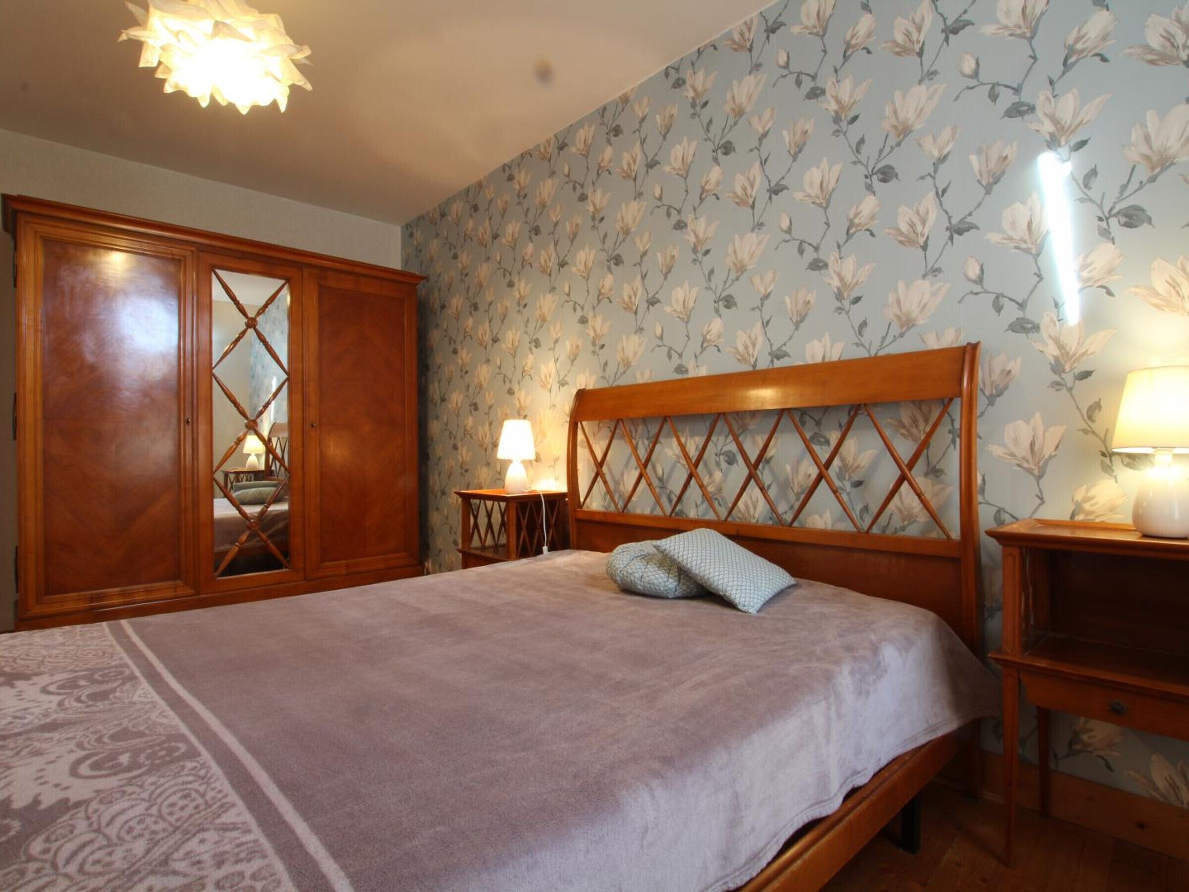 Un dormitorio con cama, armario de madera y papel tapiz floral.