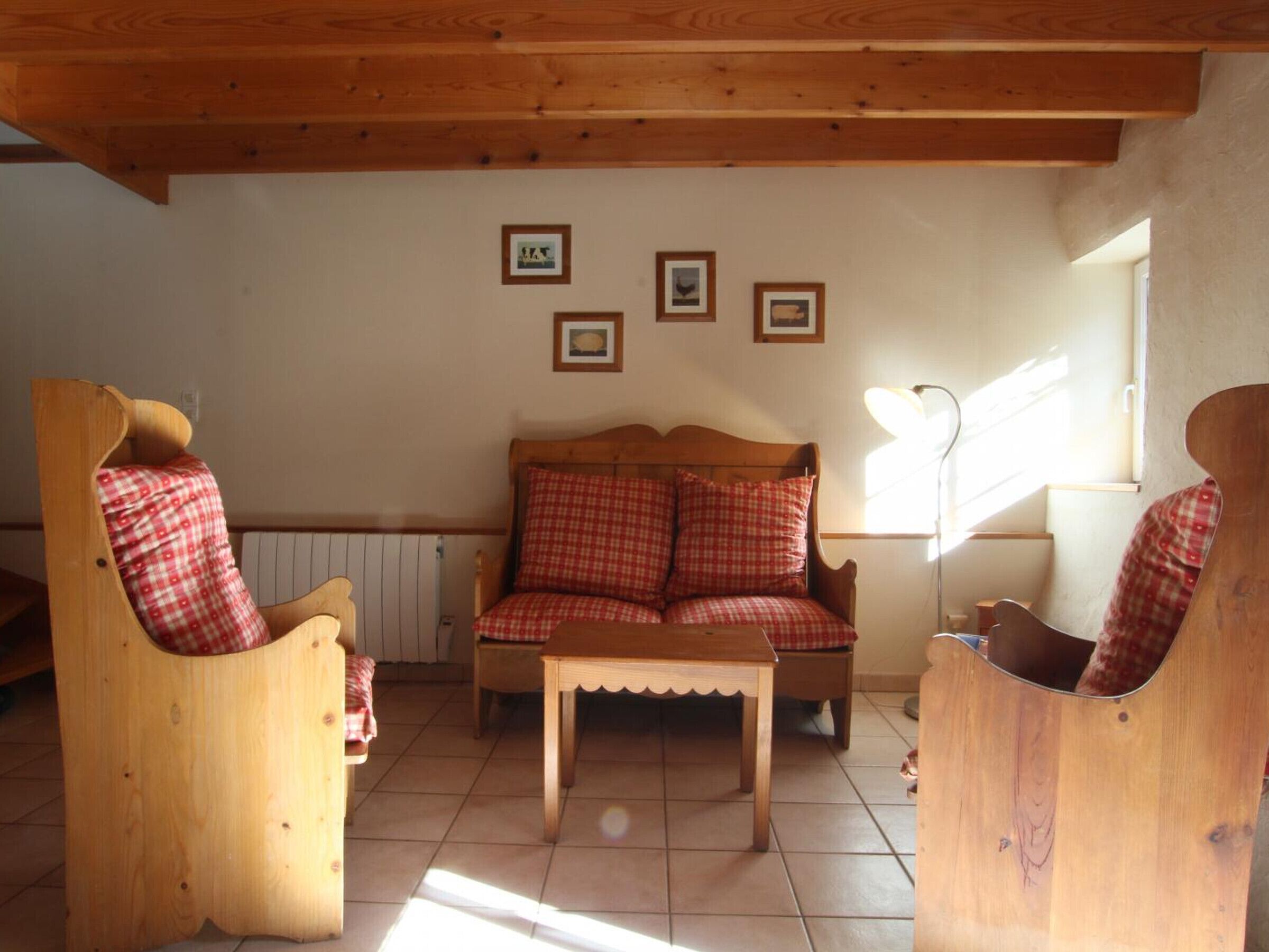 Een gezellige kamer met een houten plafond, een houten bank met geruit kussens, een houten tafel en een radiator.