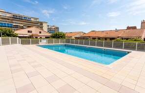 Ein rechteckiger Swimmingpool mit gefliestem Sonnendeck, umgeben von weißen Zäunen und blauem Himmel.