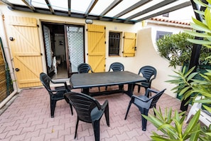 Une terrasse avec une table et des chaises, une porte jaune et une plante en pot.