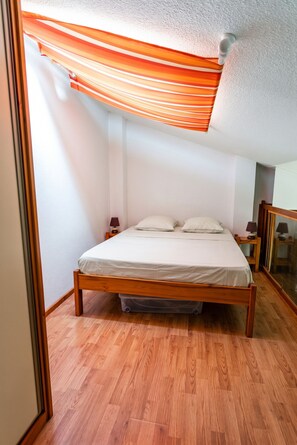 Ein Schlafzimmer mit einem hölzernen Bett, weißer Bettwäsche, einem kleinen Nachttisch mit Lampe und einem großen Spiegel an der Wand.