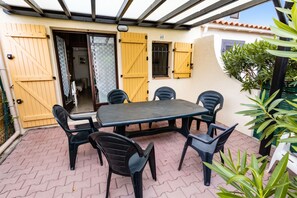 A covered patio area with a table and chairs, a door with a number sign, and a view of a building with a tiled roof.