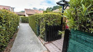 A narrow pathway flanked by neatly trimmed hedges and a black fence, leading to a residential area with houses. - Homerez - House in Argelès-sur-Mer with shared pool (Argelès-sur-Mer)