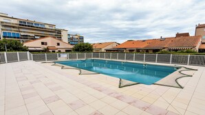 A swimming pool with a tiled deck, surrounded by a white fence, and buildings in the background. - Homerez - House in Argelès-sur-Mer with shared pool (Argelès-sur-Mer)