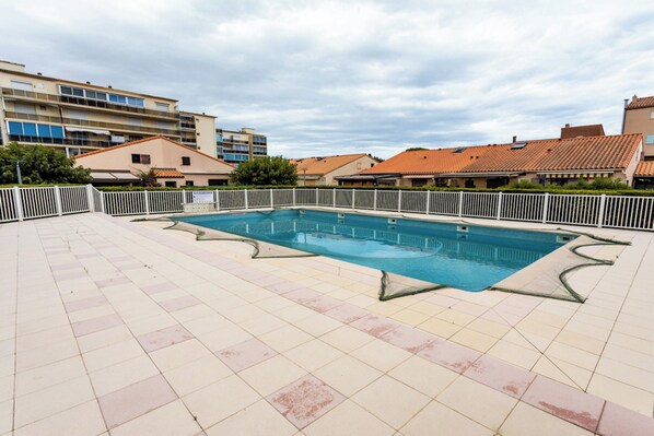 A swimming pool with a tiled deck, surrounded by a white fence, and buildings in the background. - Homerez - House in Argelès-sur-Mer with shared pool (Argelès-sur-Mer)