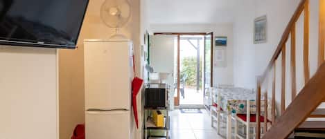 A compact kitchen with a refrigerator, a microwave, and a fan. There's a dining area with a table and chairs, and a staircase leading upstairs.