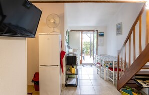 A compact kitchen with a refrigerator, a microwave, and a fan. There's a dining area with a table and chairs, and a staircase leading upstairs.