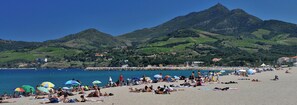 A beach with people sunbathing and swimming, surrounded by green hills and a clear blue sky. - Homerez - House in Argelès-sur-Mer with shared pool (Argelès-sur-Mer)
