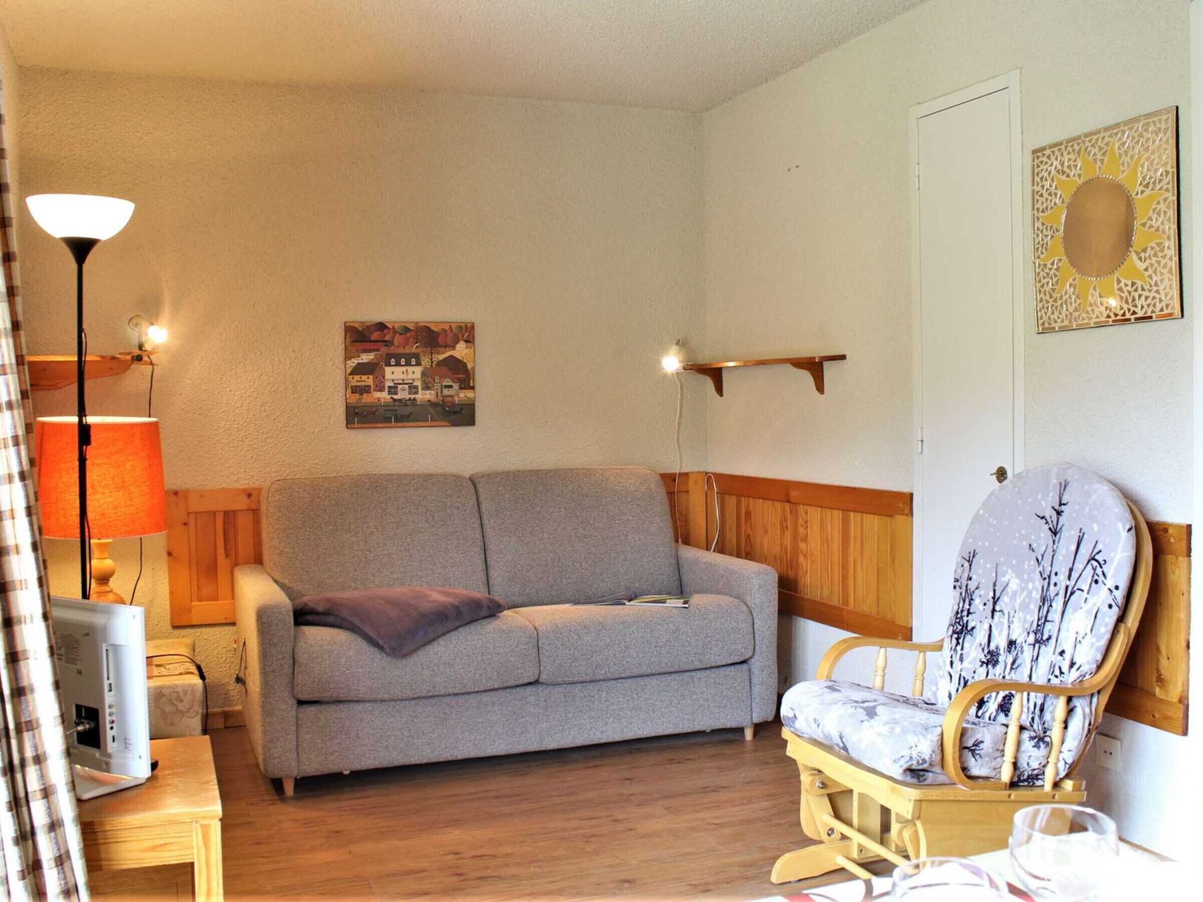 Un salon chaleureux avec un canapé gris, une chaise en bois, une lampe et un tableau accroché au mur.