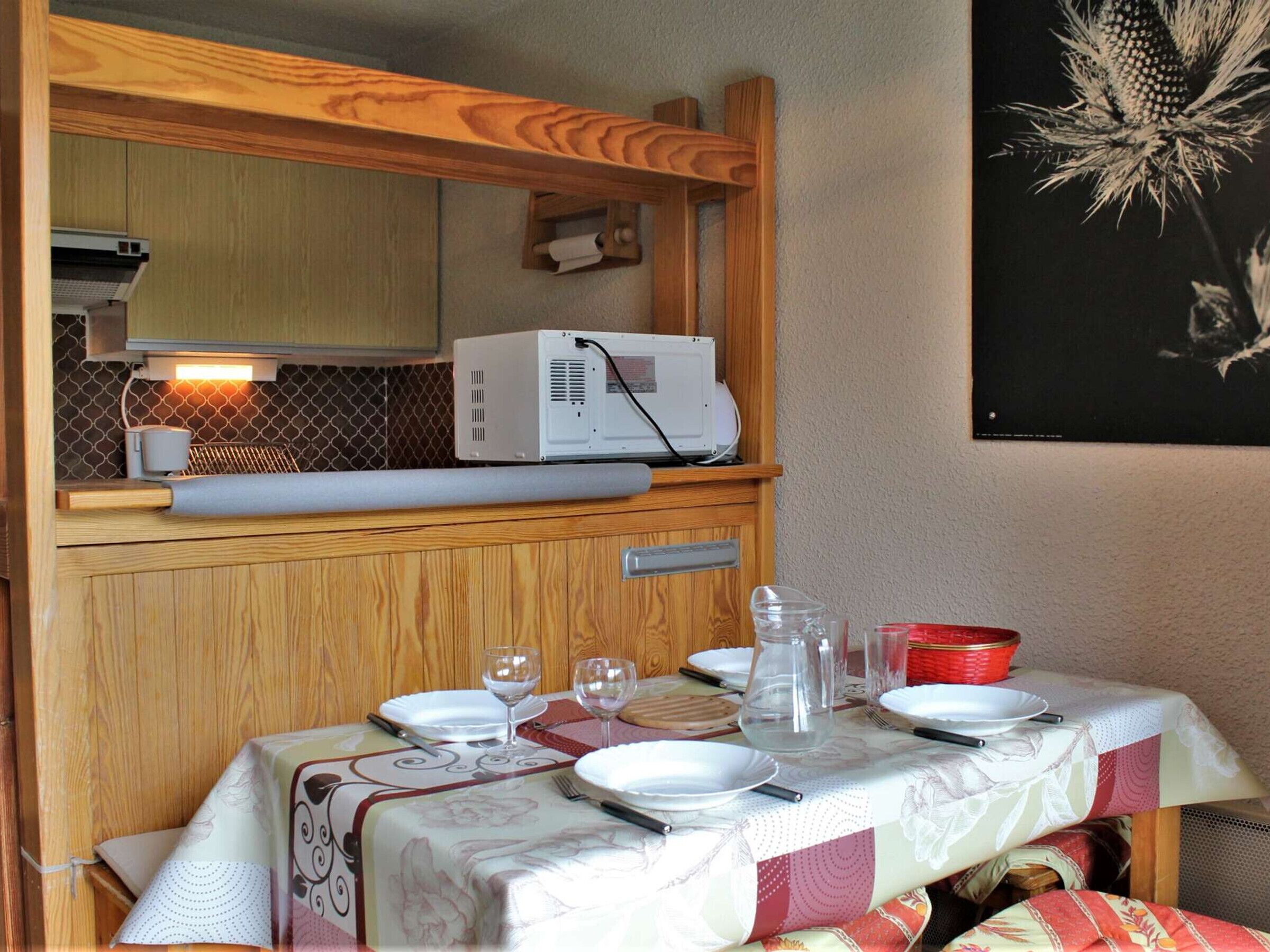 A compact kitchenette with a microwave, a small oven, and a coffee maker. There is a table set with plates, glasses, and cutlery.
