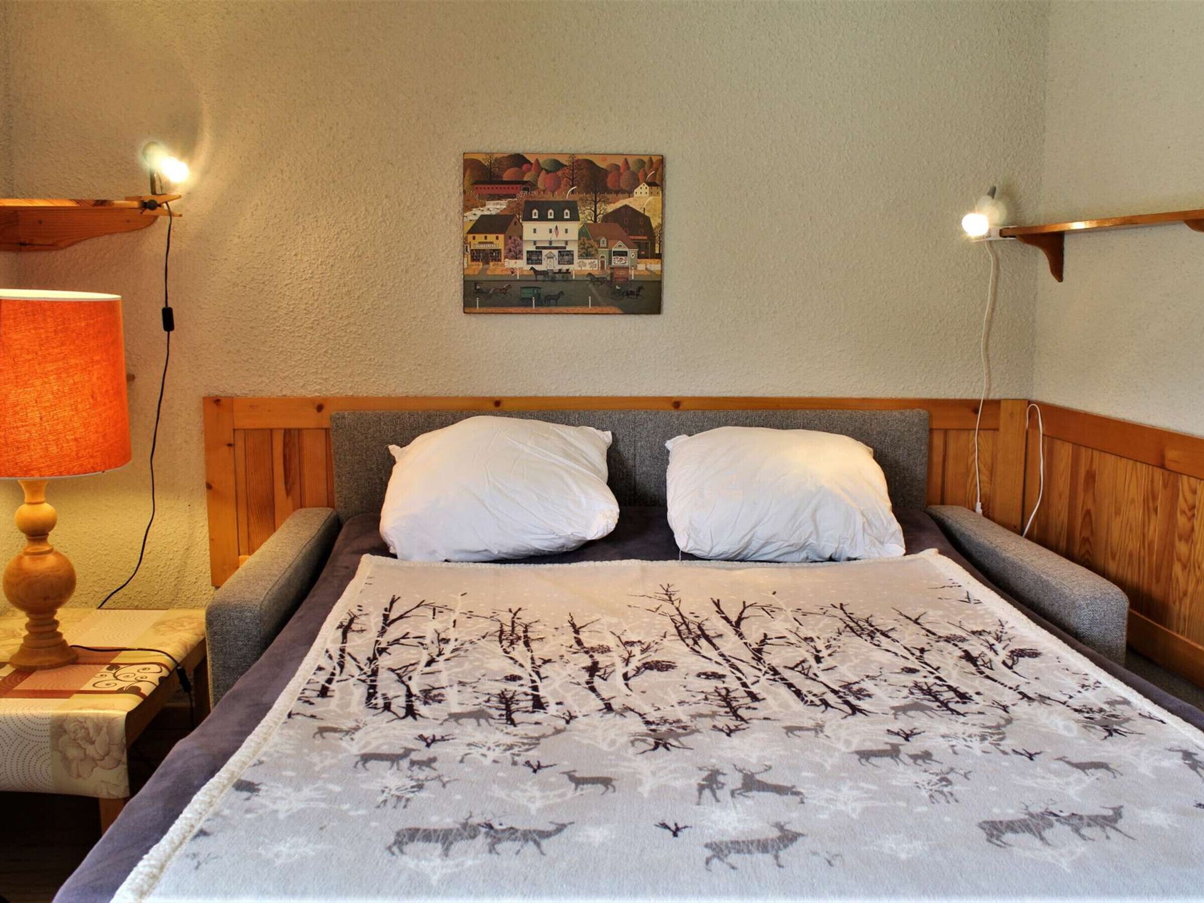 Une chambre à coucher avec un lit, deux oreillers, une table de chevet avec une lampe, un tableau accroché au mur et une tête de lit en bois.