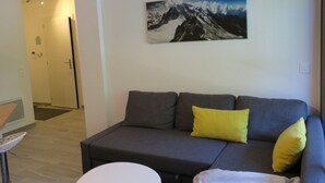 Un salón moderno con un sofá gris, una mesa redonda blanca y una pintura de un paisaje montañoso en la pared.