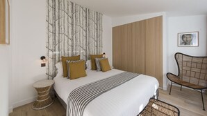 A bedroom with a large bed, a wall-mounted artwork of trees, a wooden wardrobe, a wicker chair, and a small side table. - Balthazar, 4BR/4BA, 9 people (París)