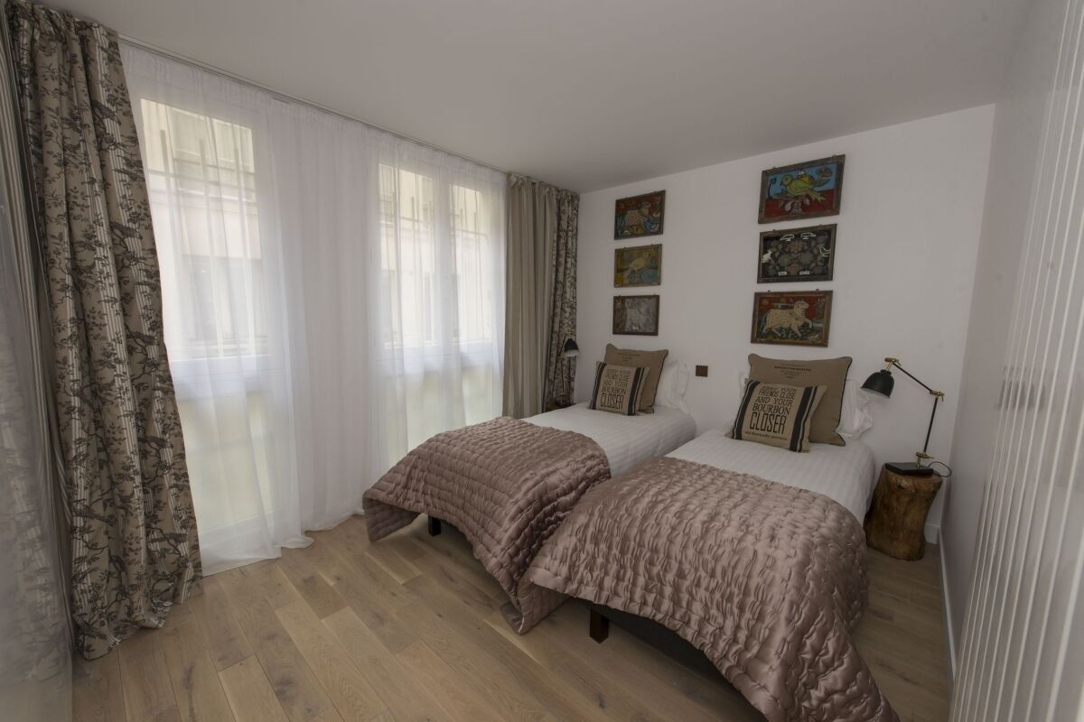 Un dormitorio con dos camas, suelo de madera y una ventana con cortinas translúcidas.