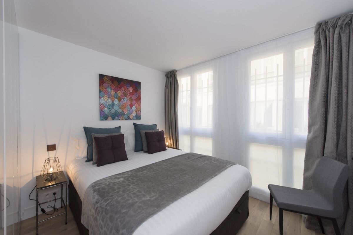 Een moderne hotelkamer met een groot bed, een stoel, een nachtkastje en een raam met gordijnen.
