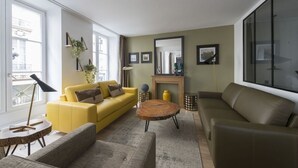 A modern living room with a yellow sofa, a brown sofa, a round wooden coffee table, and a fireplace. - Balthazar, 4BR/4BA, 9 people (París)
