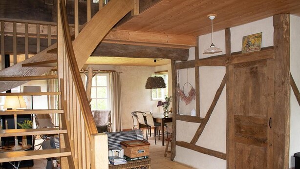 A rustic interior with exposed wooden beams, a staircase, a dining area with a checkered tablecloth, and a large wooden door. - Charming eco-gîte, no TV or internet, pets welcome (La Mouche)